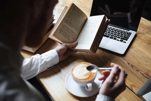 Foto gratuita vista superior del hombre en camisa blanca revolviendo café mientras lee el libro